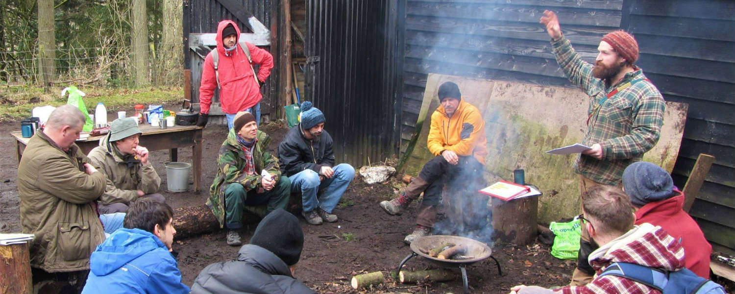 Group around a fire in the woods listening to instructor