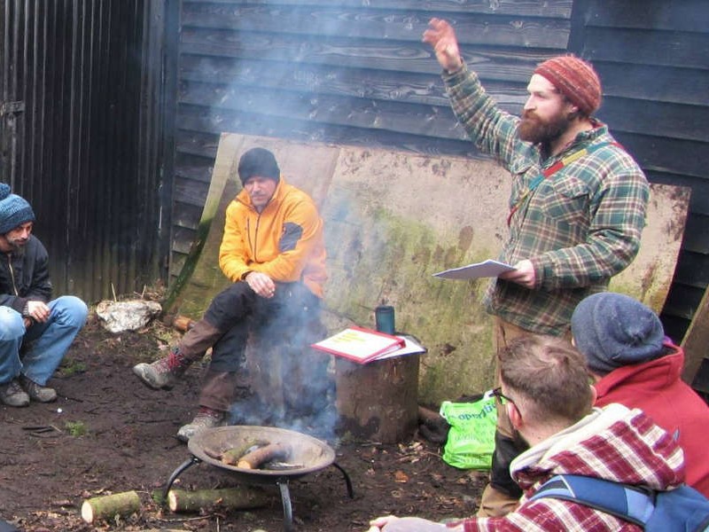 Group around a fire in the woods listening to instructor