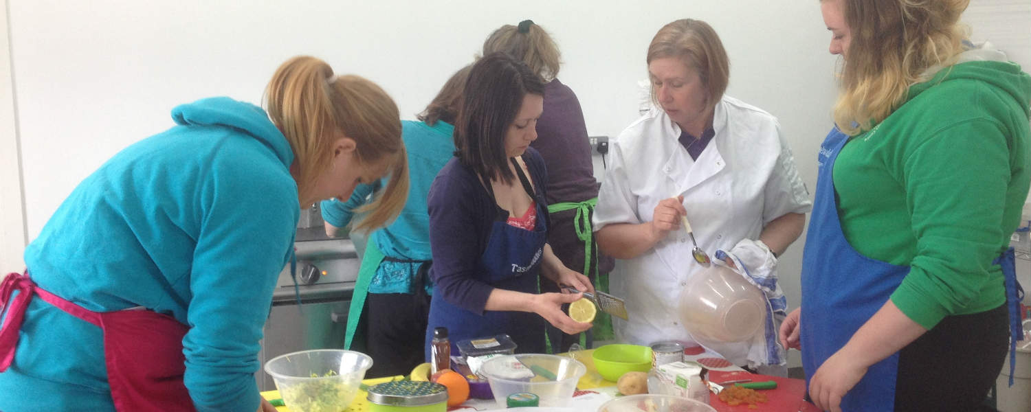 Mums preparing food in a training kitchen with Chef giving instructions